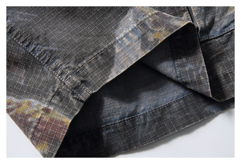 Close-up of the stitched hem on dark gray plaid trousers with muted colored accents.