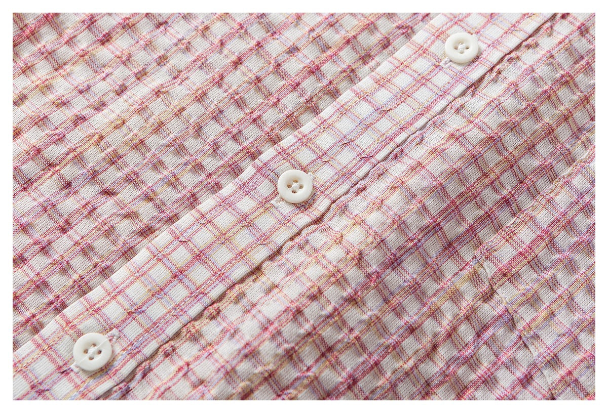 Close-up of a cream plaid garment placket with three white buttons and pink, red, and yellow lines.