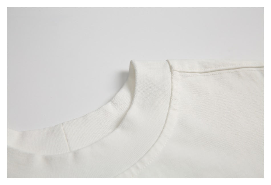Close-up of the ribbed crew neckline and shoulder seam of an off-white T-shirt.