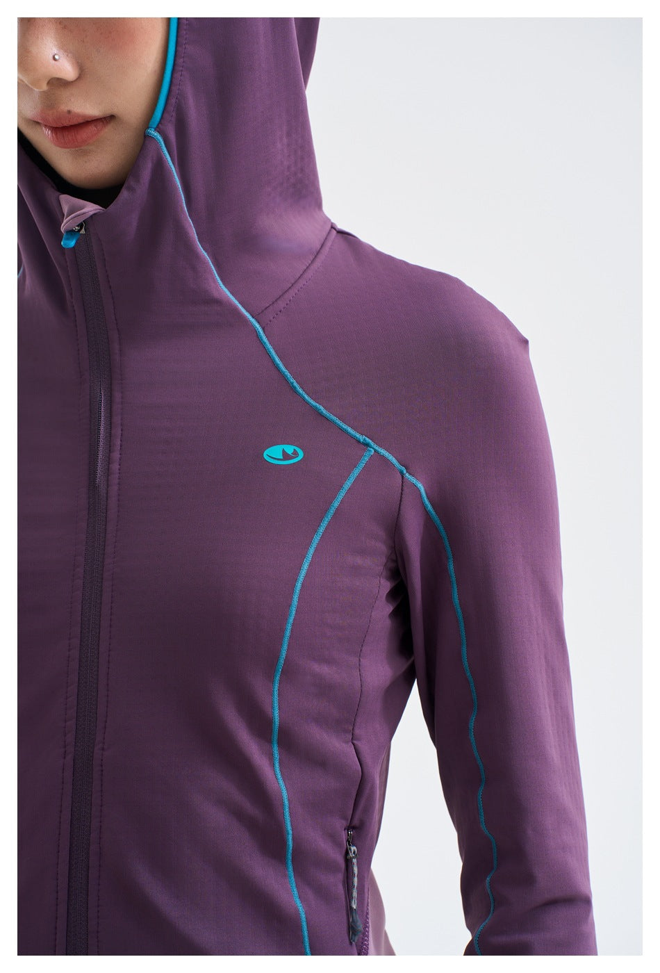 Close-up of a purple hooded jacket showing turquoise piping, a chest emblem, front zipper and side pocket.