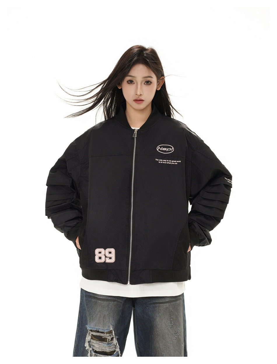 Model with hands in pockets wearing a black zip bomber jacket with pleated sleeves and pink 89 patch