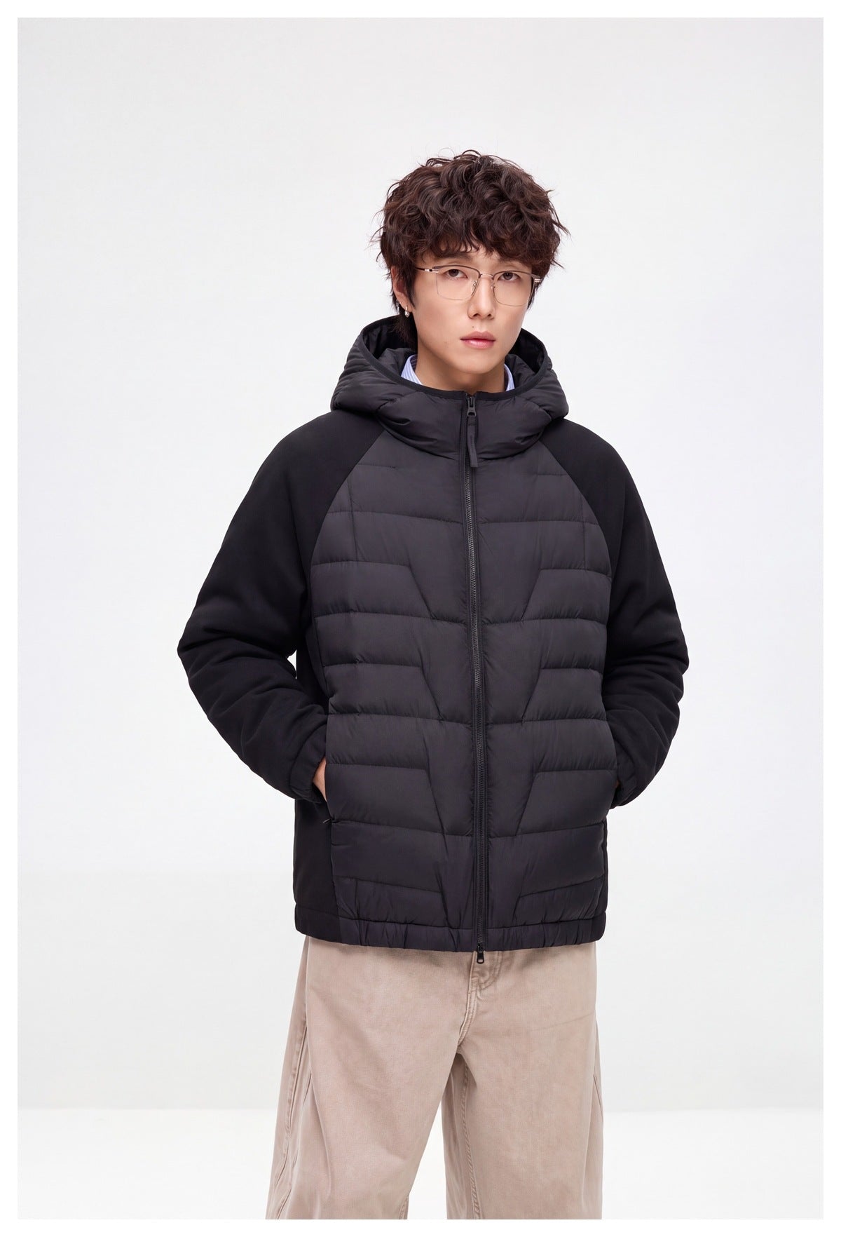 Model wearing a black hooded jacket with a horizontally quilted front and solid raglan sleeves.