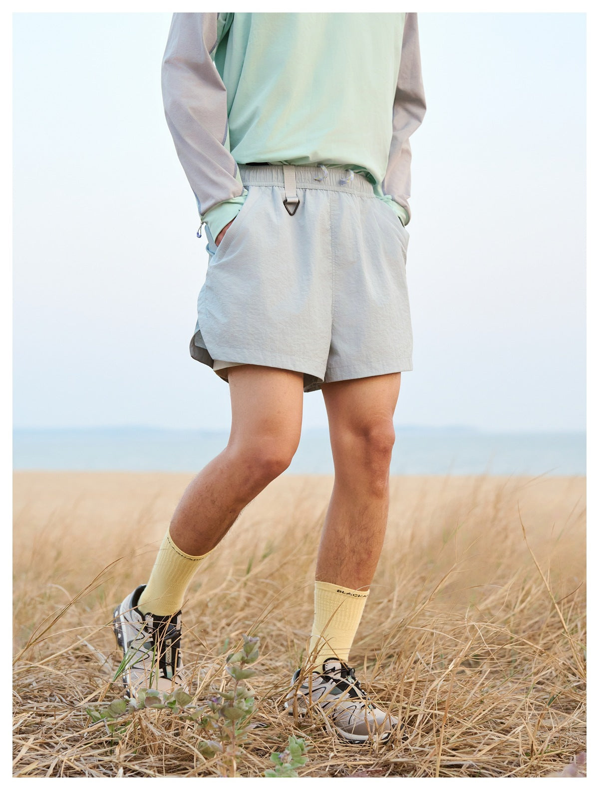 Close view of light gray shorts with an elastic drawstring waist, worn with a mint-and-gray shirt.