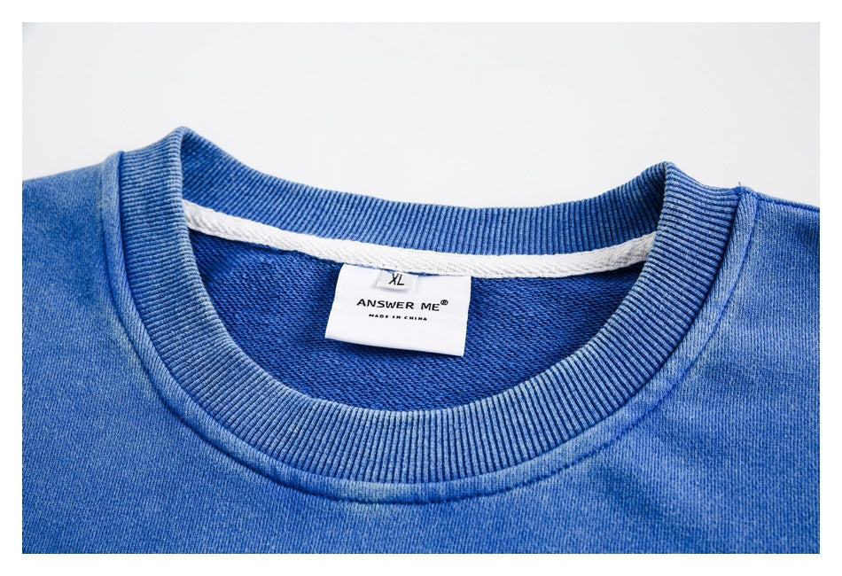 Close-up of a blue sweatshirt's ribbed crew neckline and inner label reading ANSWER ME and MADE IN CHINA.