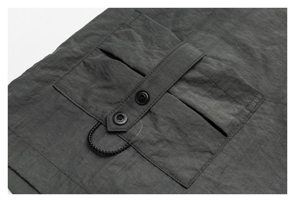 Close-up of a charcoal-gray pocket with a buttoned tab and looped cord detail.