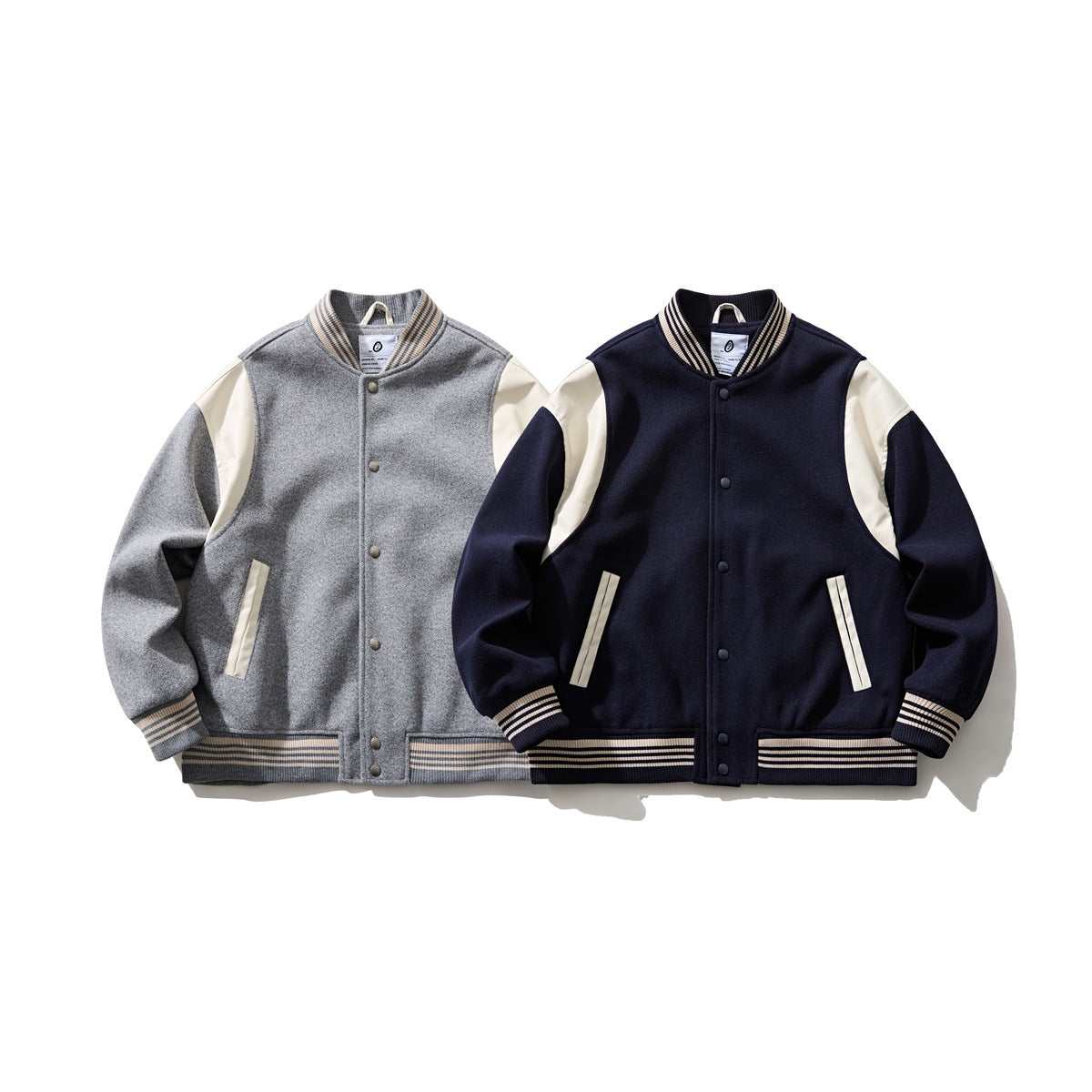 Two front-facing varsity jackets: one gray with cream accents and one navy with cream accents; both have striped trim.