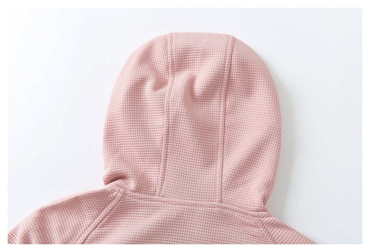 Close-up of the pale pink jacket's textured hood and stitched panel seams, laid flat.