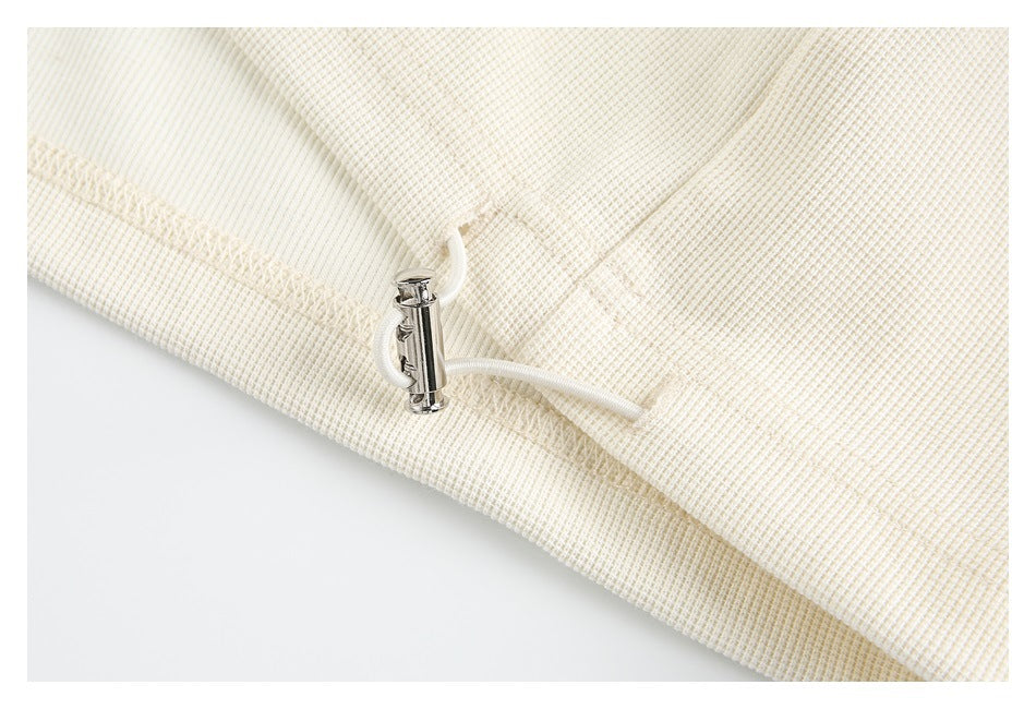 Close-up of a cream drawcord and small silver toggle at the garment's edge.