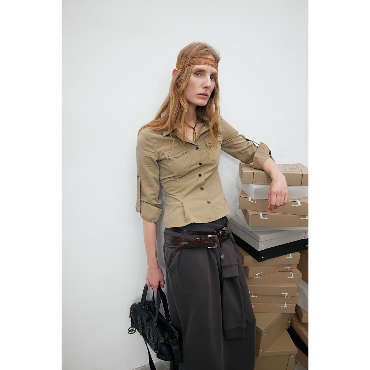 Model wears a fitted khaki button-up shirt with two flap chest pockets and rolled sleeves.