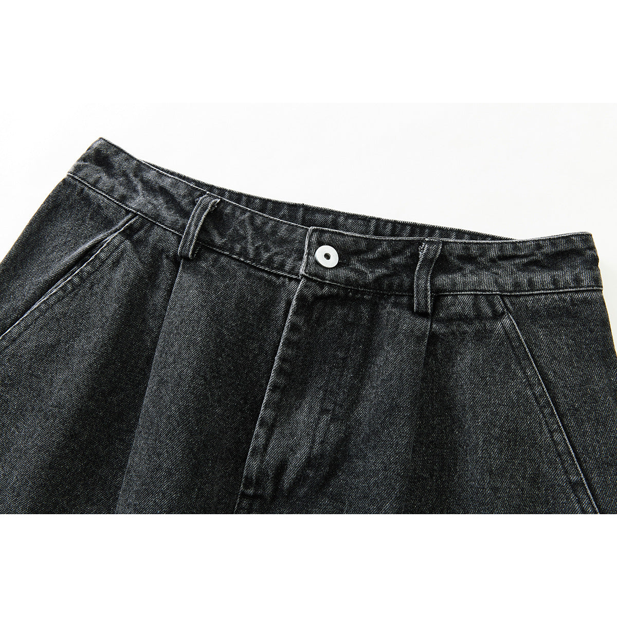 Close-up of black washed denim trousers showing the front waistband, white button, belt loops and pleated front.