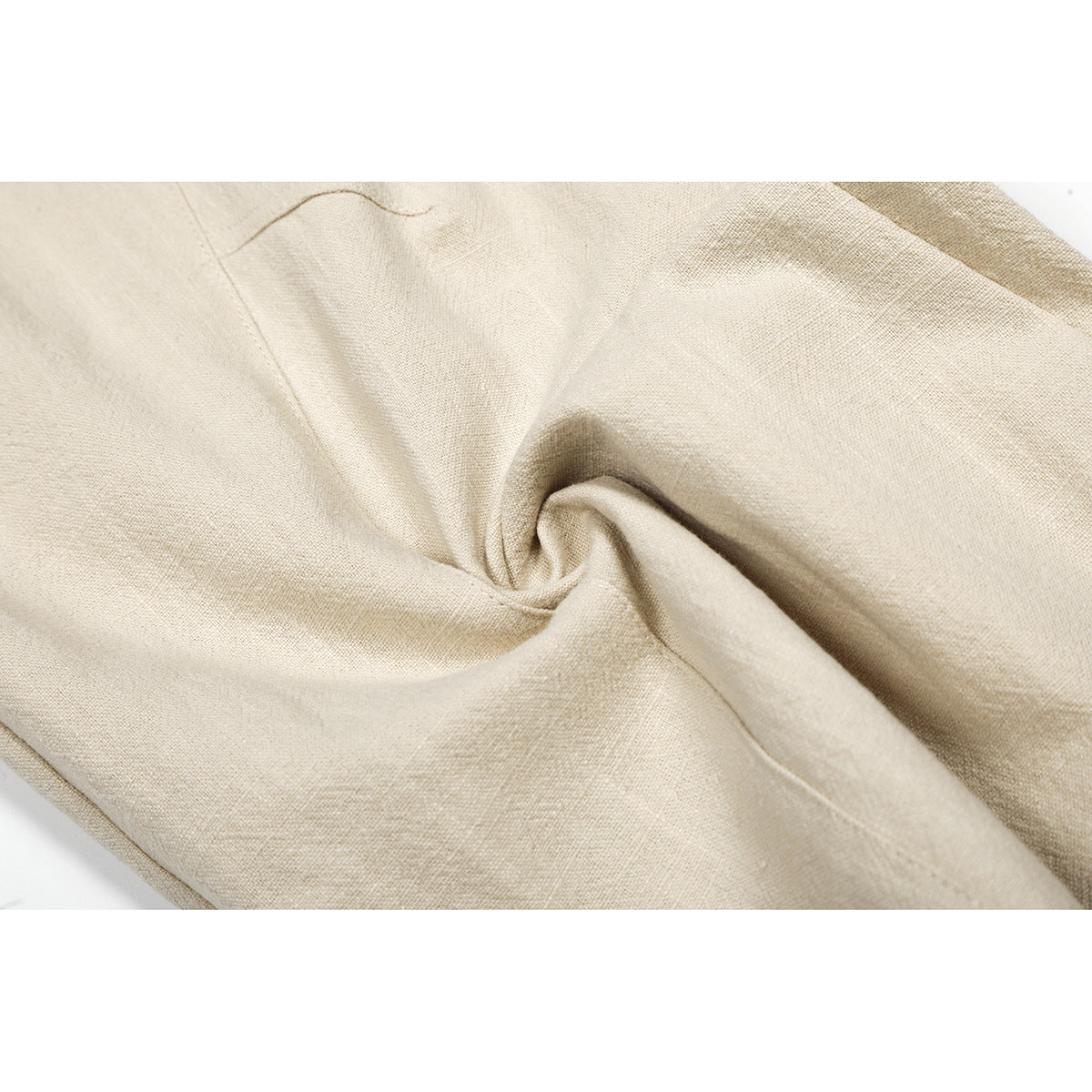 Close-up of beige trouser fabric gathered into folds, showing its woven texture and stitching.