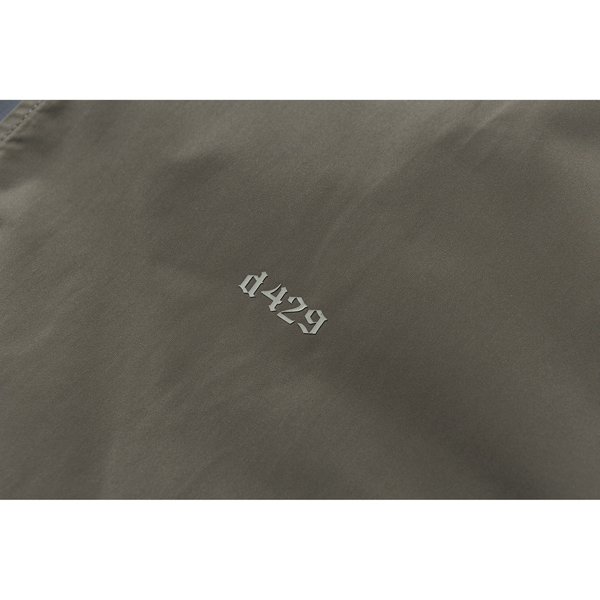 Close-up of olive-gray jacket fabric with a small raised silver “0429” marking.