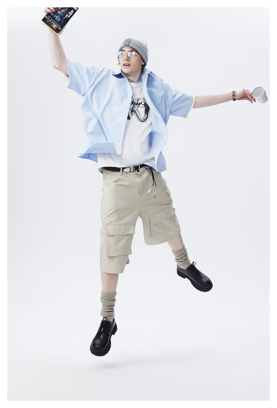 Model jumping in a light blue short-sleeve shirt and beige cargo shorts, with arms spread wide.