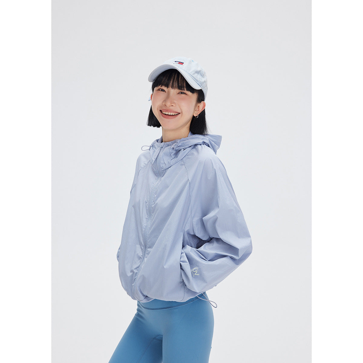 Model wearing a pale blue hooded zip jacket and blue leggings, shown from the front against a white background.