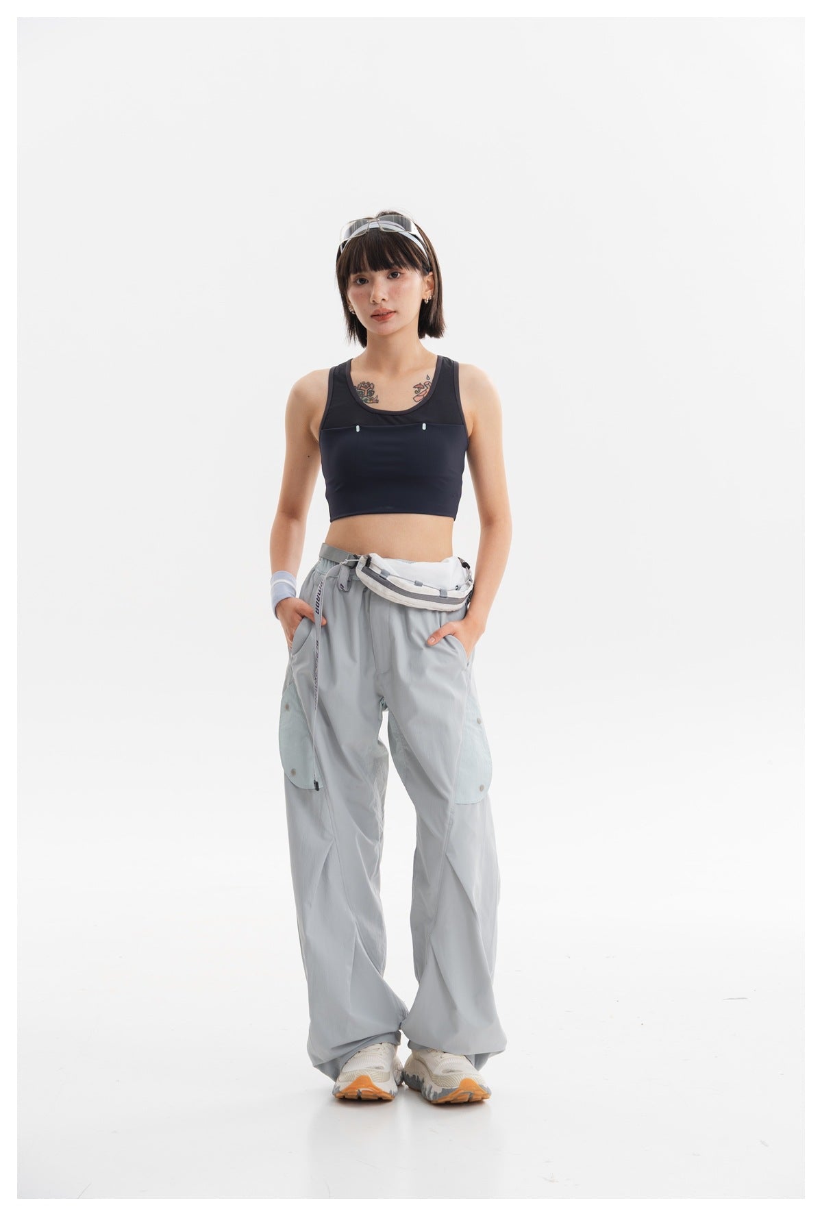 Full-length model wearing a navy cropped tank and loose pale blue-gray cargo pants with a white waist pouch.