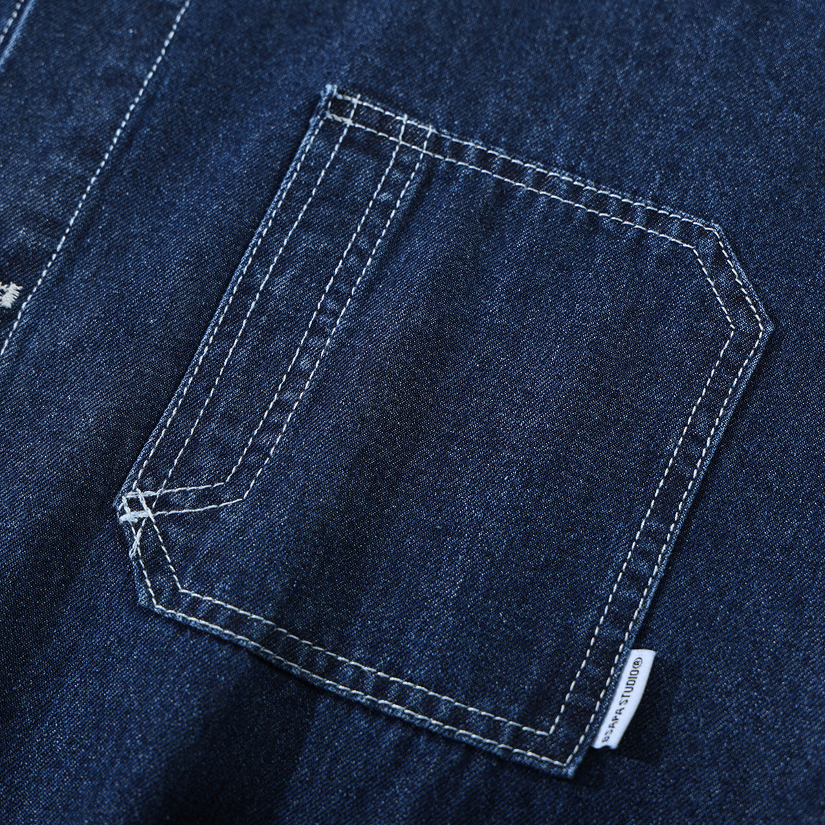 Close-up of a dark indigo denim shirt pocket with contrasting white stitching and a small side label.