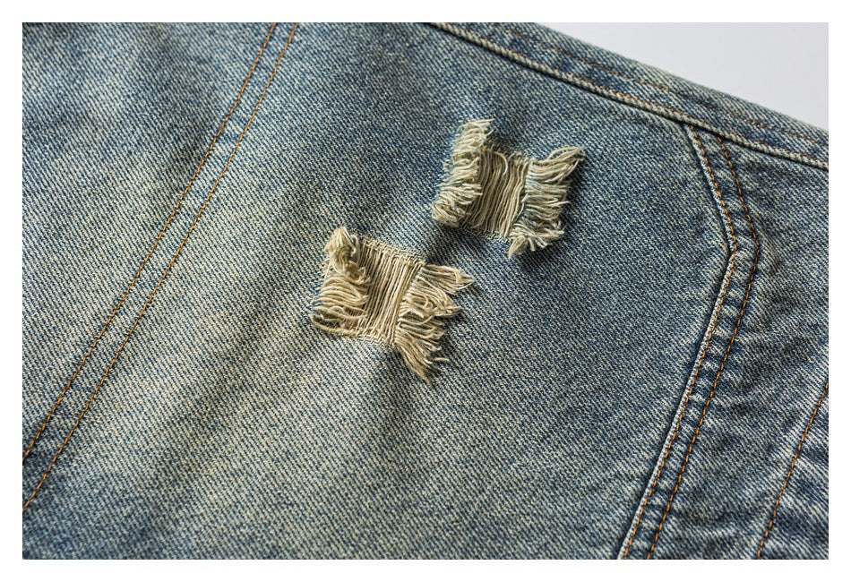 Close-up of two frayed distressed patches on washed blue denim between orange-stitched seams.