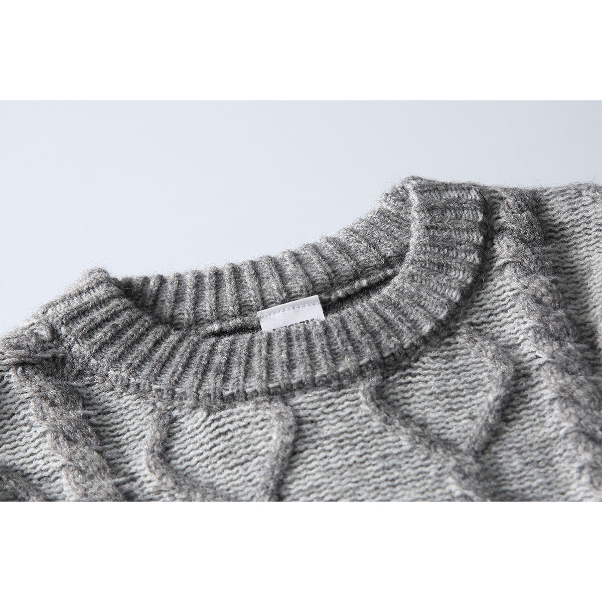 Close-up of a gray cable-knit sweater's ribbed crew neckline and small blank label.
