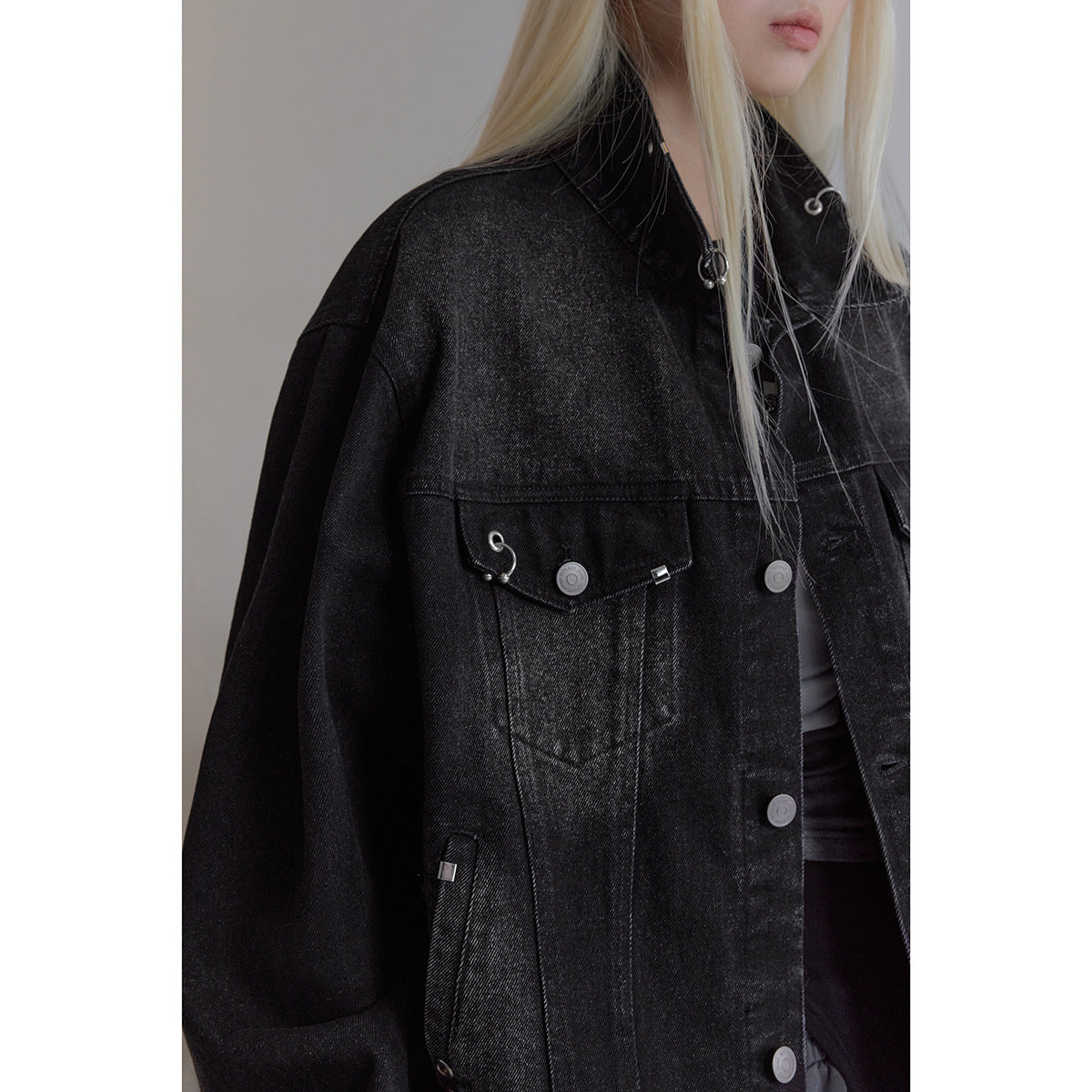 Close-up of the black denim jacket's chest pocket, buttons, seams, and silver hardware.