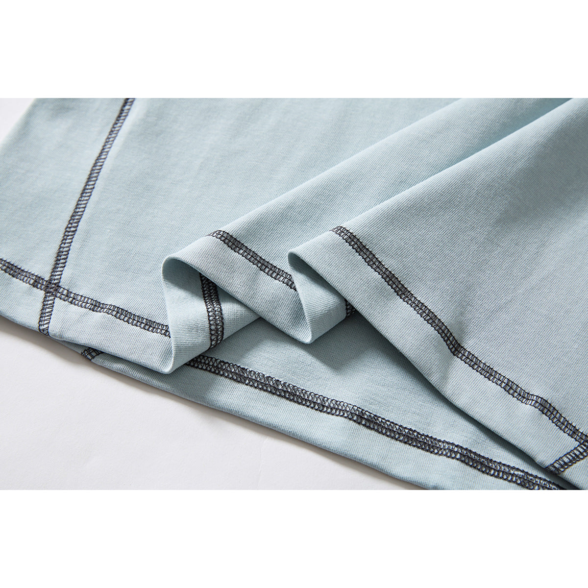 Close-up of pale blue T-shirt fabric folded to show dark overlock stitching along the hem and seams.