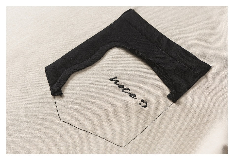 Close-up of a cream chest pocket with an irregular black fabric trim and small black script embroidery.