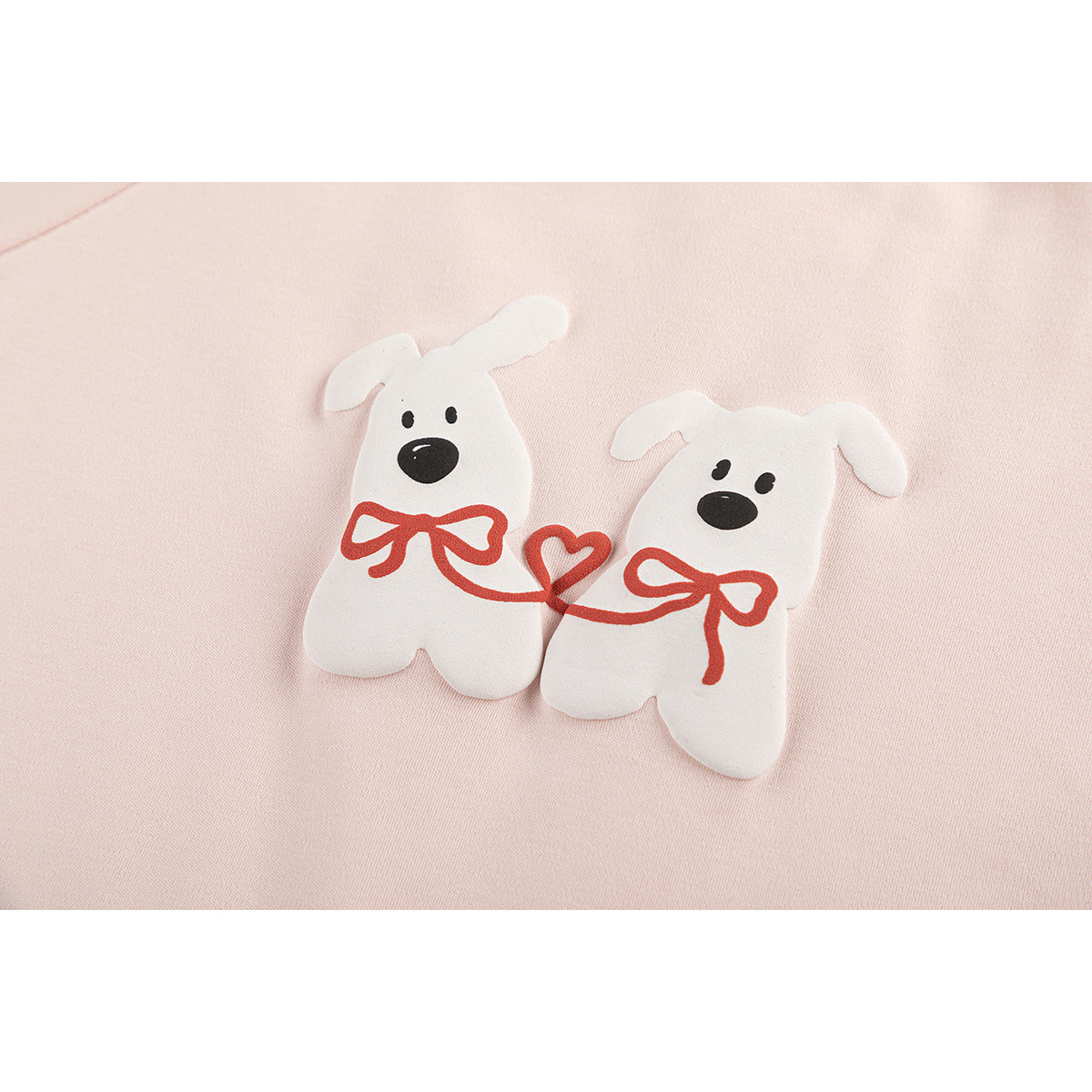 Close-up of a pale pink shirt showing two white dog appliqués linked by red bows and a heart.