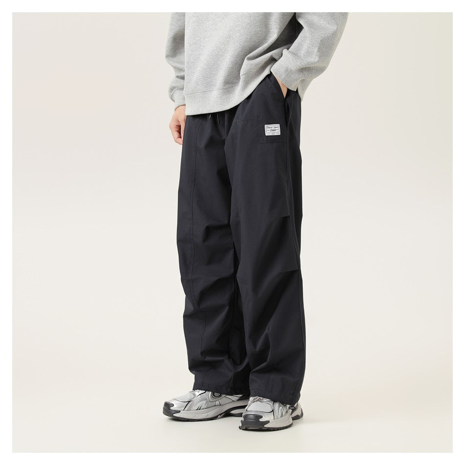 Front view of a person wearing black-blue wide-leg pants with a thigh patch, gray sweatshirt and sneakers