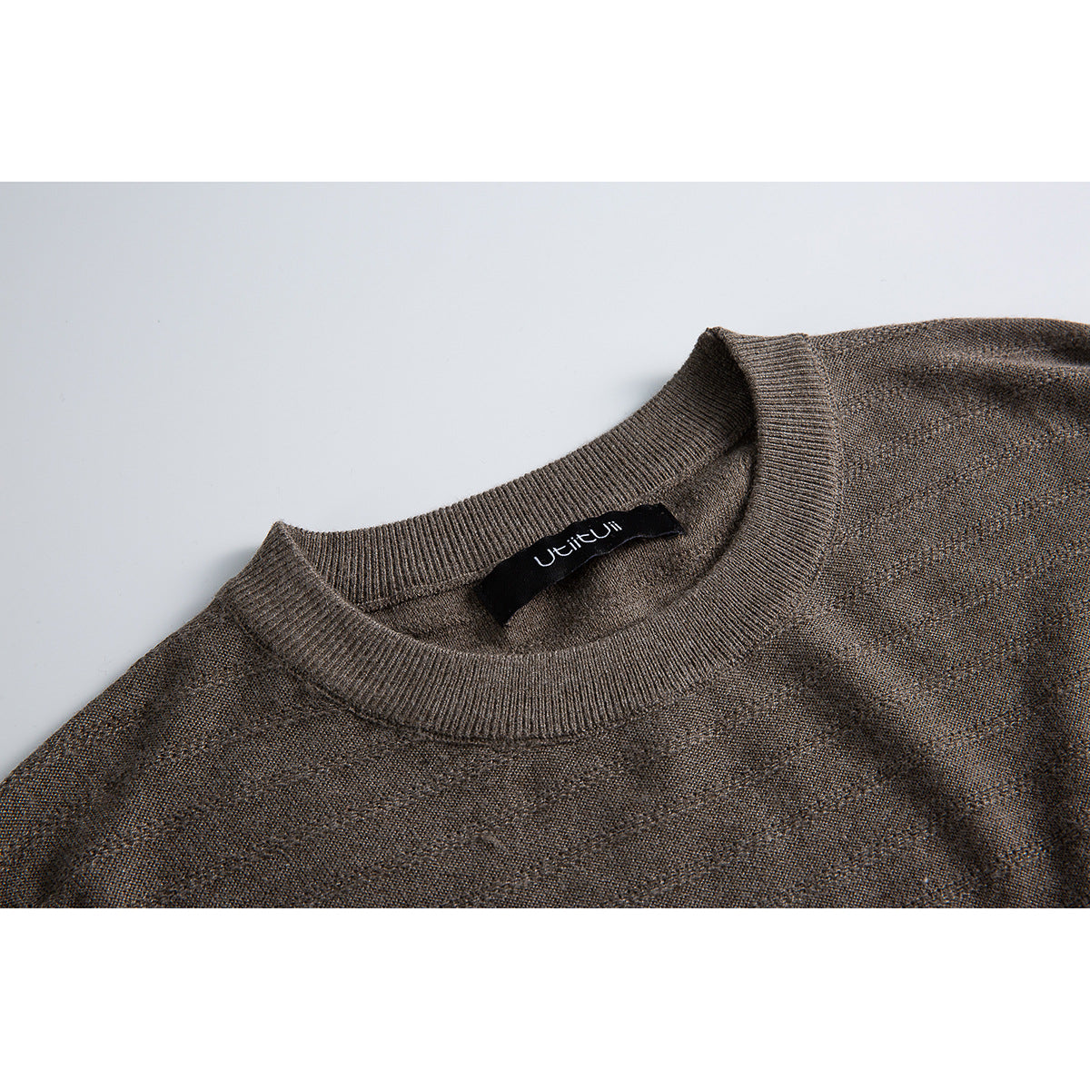 Close-up of a brown-gray knit sweater's ribbed crew neckline and inner neck label.