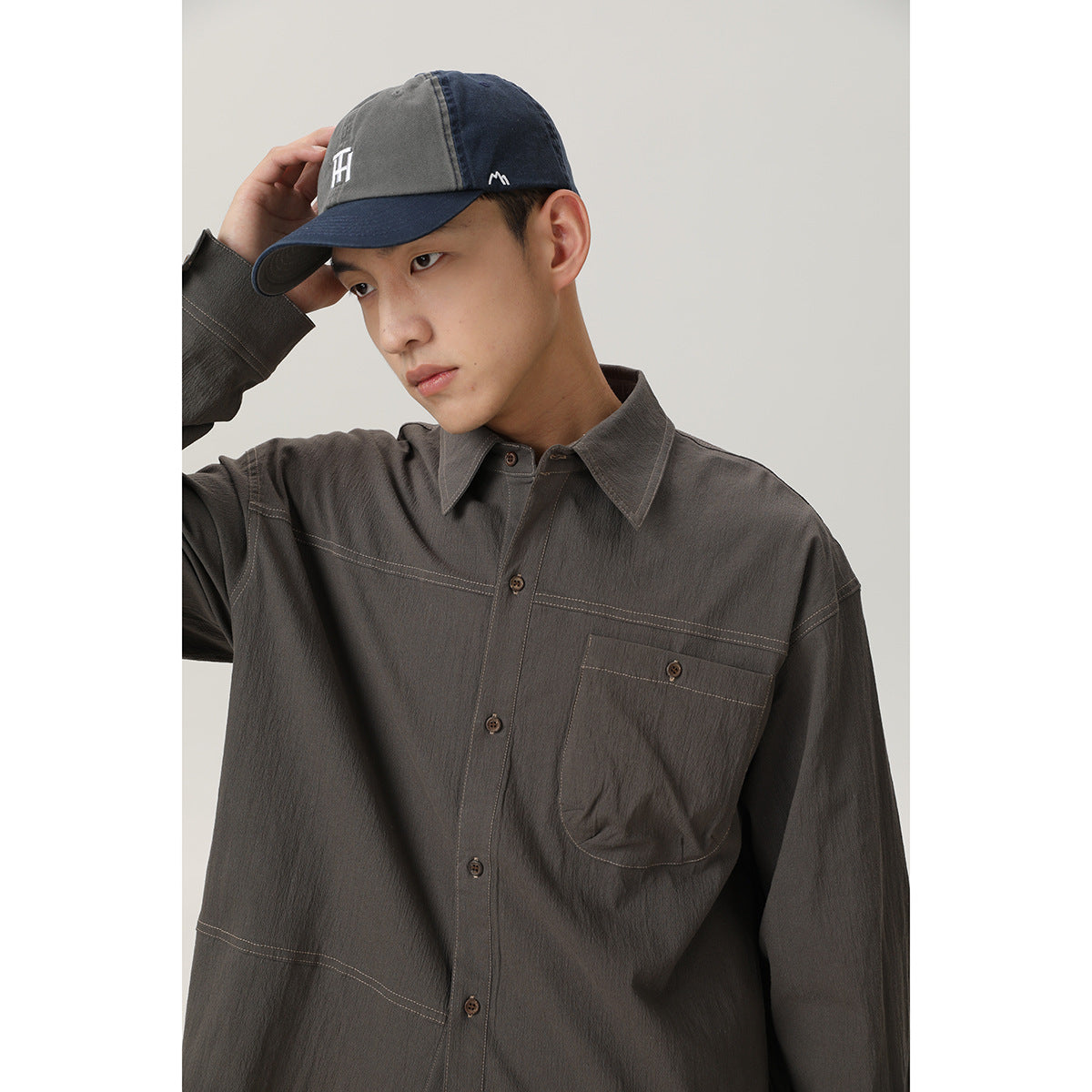 Close view of a man wearing a charcoal gray button-up shirt with contrast stitching and a single chest pocket.