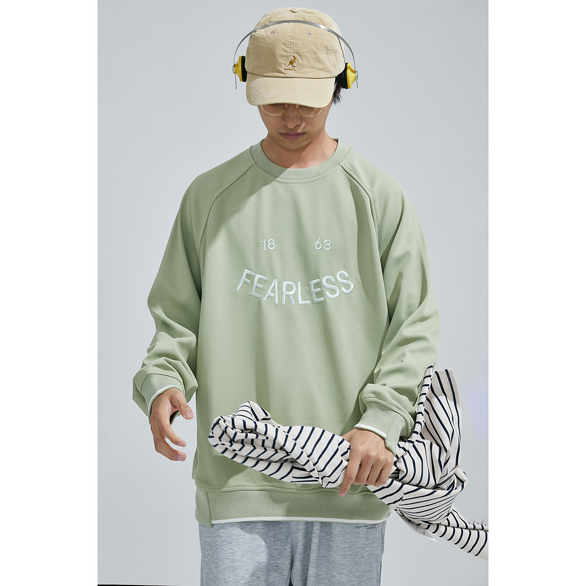 Front view of a model wearing a sage green sweatshirt with white FEARLESS lettering and gray pants.