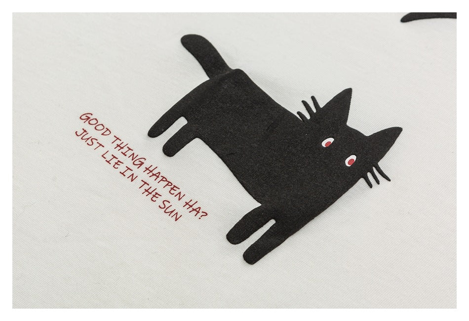 Close-up of a black cat graphic and red lettering reading “GOOD THING HAPPEN HA? JUST LET IN THE SUN” on ivory fabric.