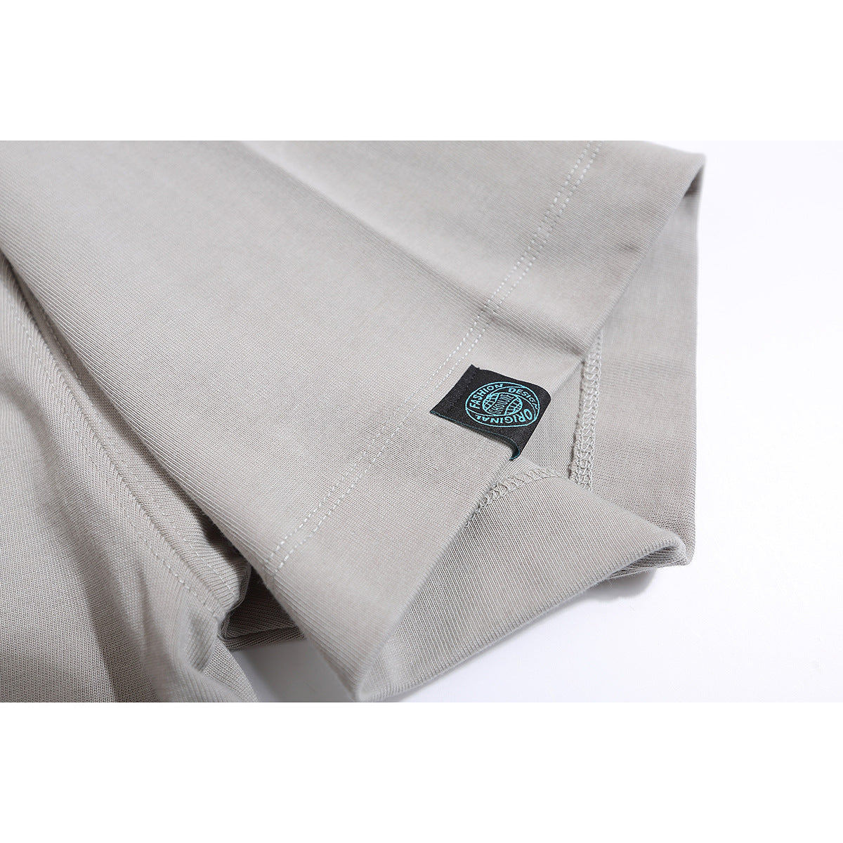 Close-up of a light gray T-shirt hem with double stitching and a small black sewn-on label.