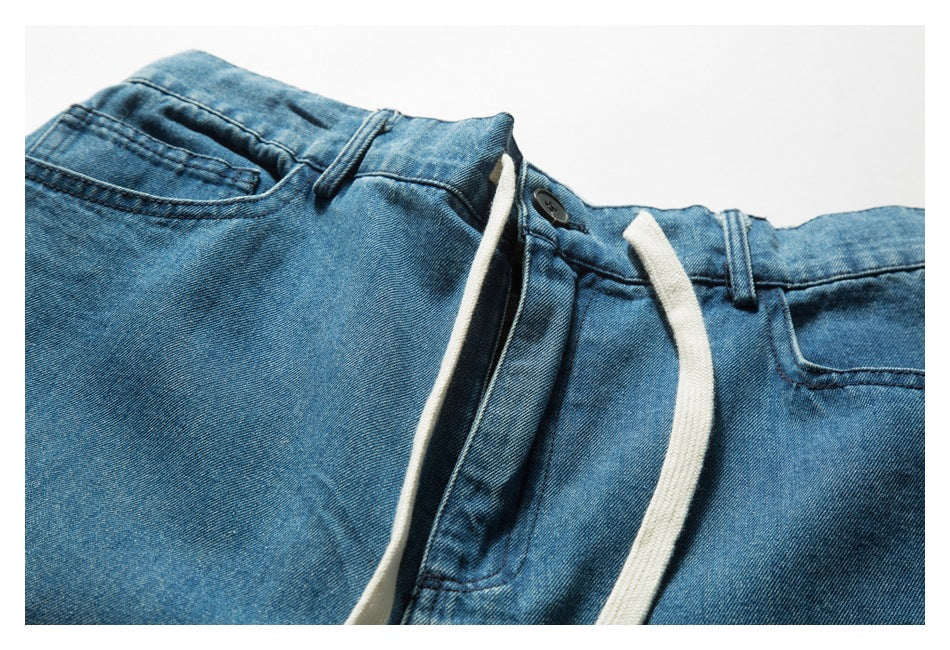 Close-up of blue denim shorts showing the front waistband, button, belt loops, pockets and white drawstrings.
