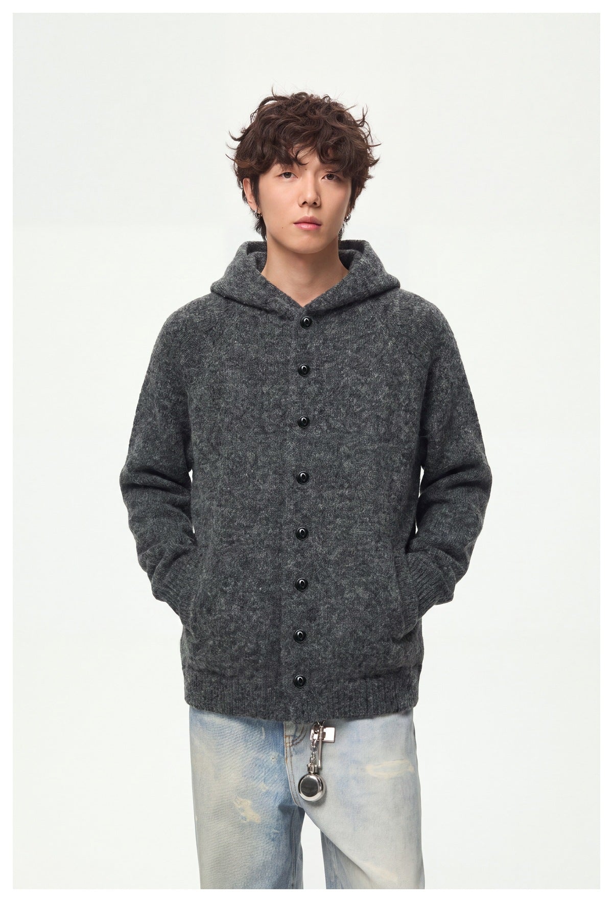 Front view of a model wearing a charcoal gray knit hooded cardigan with black buttons and light-wash jeans.