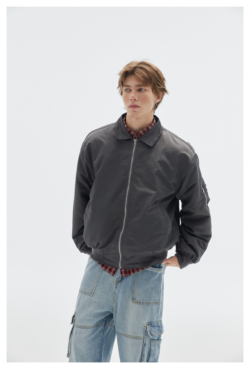 Model wearing a charcoal gray zip-front jacket with a pointed collar and zip sleeve pocket, paired with cargo jeans.