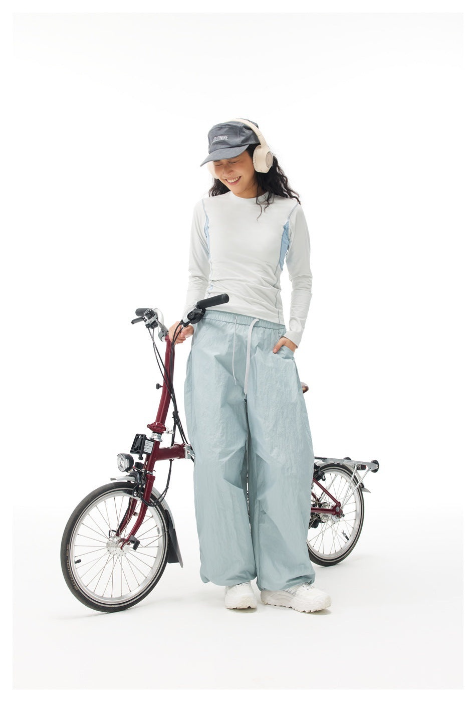 Person wearing a white long-sleeve top with light blue side panels, standing beside a maroon folding bicycle