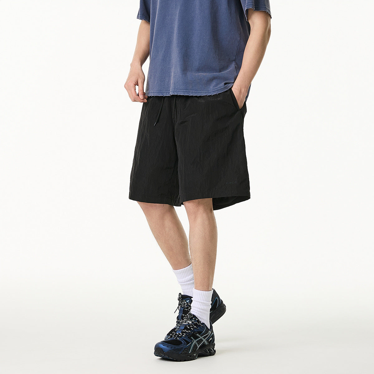 Cropped model wearing black drawstring shorts with side pockets and a blue T-shirt, shown from the front at an angle.
