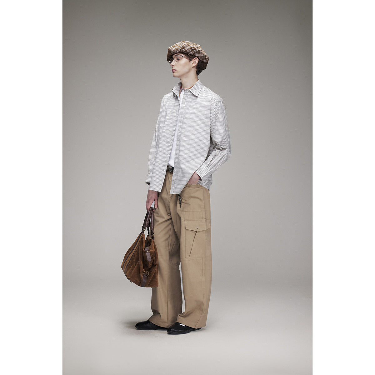 Full-length model in an oversized light gray checked shirt and tan cargo trousers, shown in profile with a brown bag.