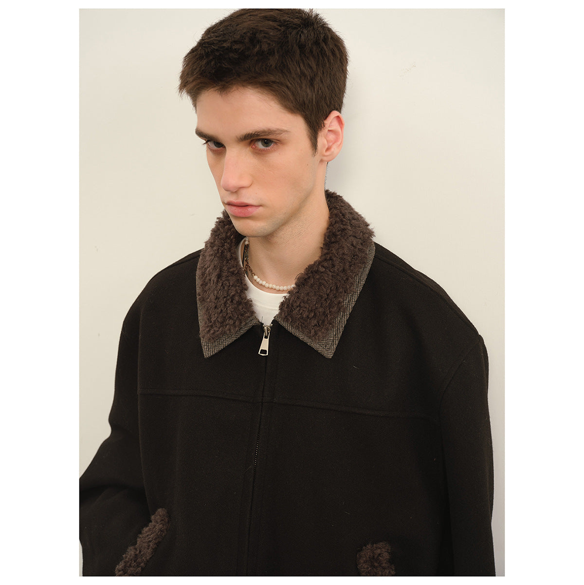 Close view of a black jacket with a brown textured collar, checked collar edging, and a silver zipper.