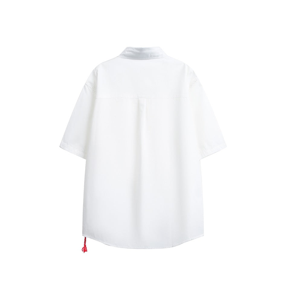 White short-sleeve shirt, back view, with back yoke, center pleat and small red tassel at the hem