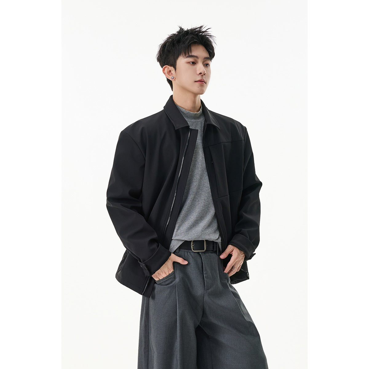 Model wearing a black zip-front jacket with a pointed collar over a gray top and dark gray trousers.
