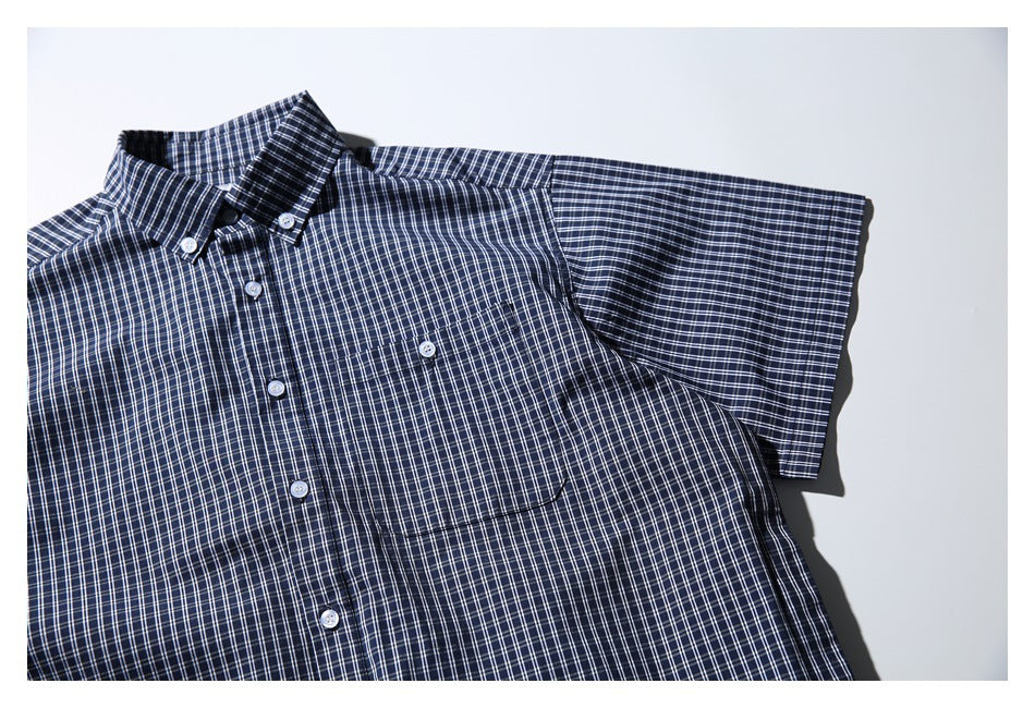 Angled close view of a navy-and-white checked shirt showing its button-down collar, placket, chest pocket, and short sleeve.