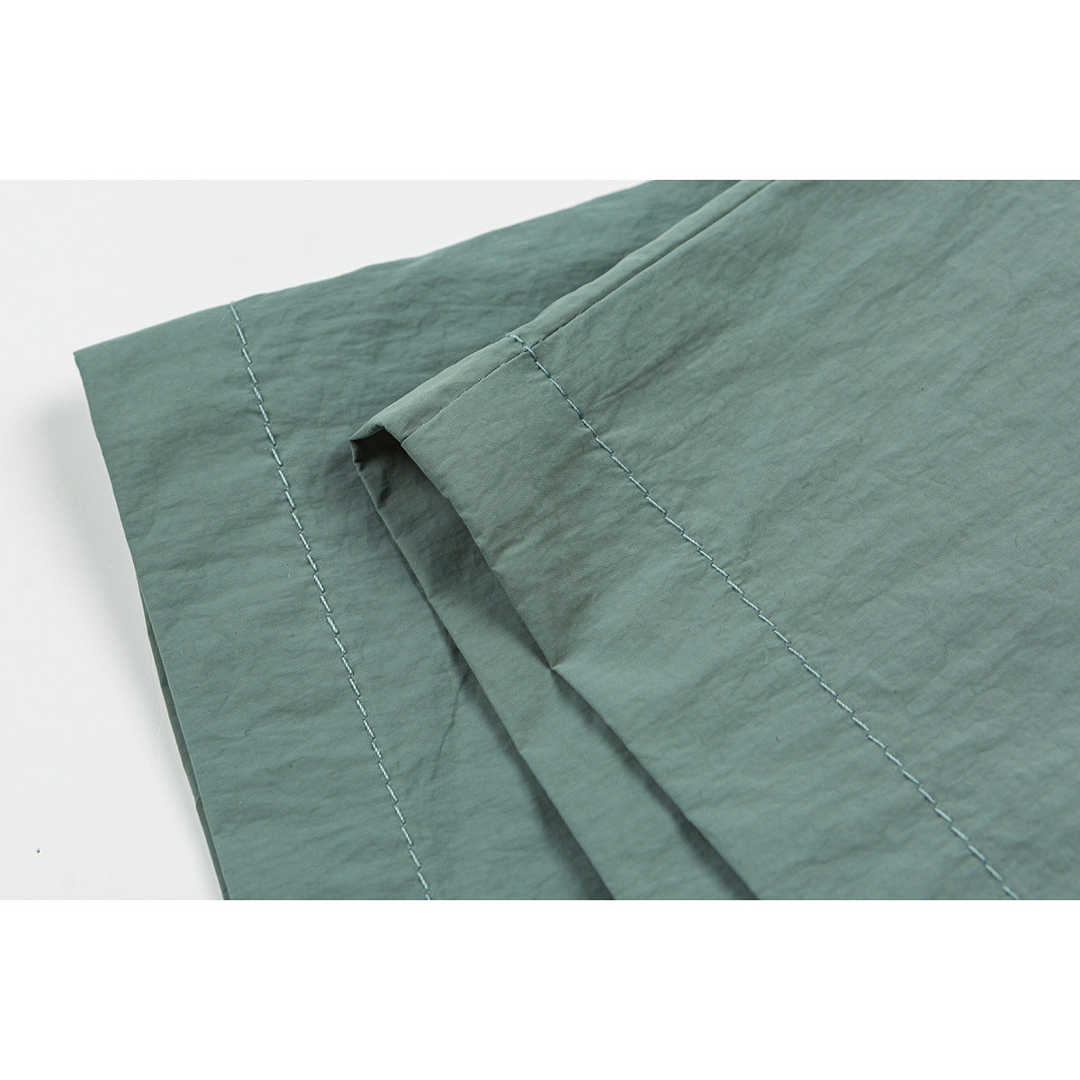 Close-up of sage green shorts fabric and stitched hem.