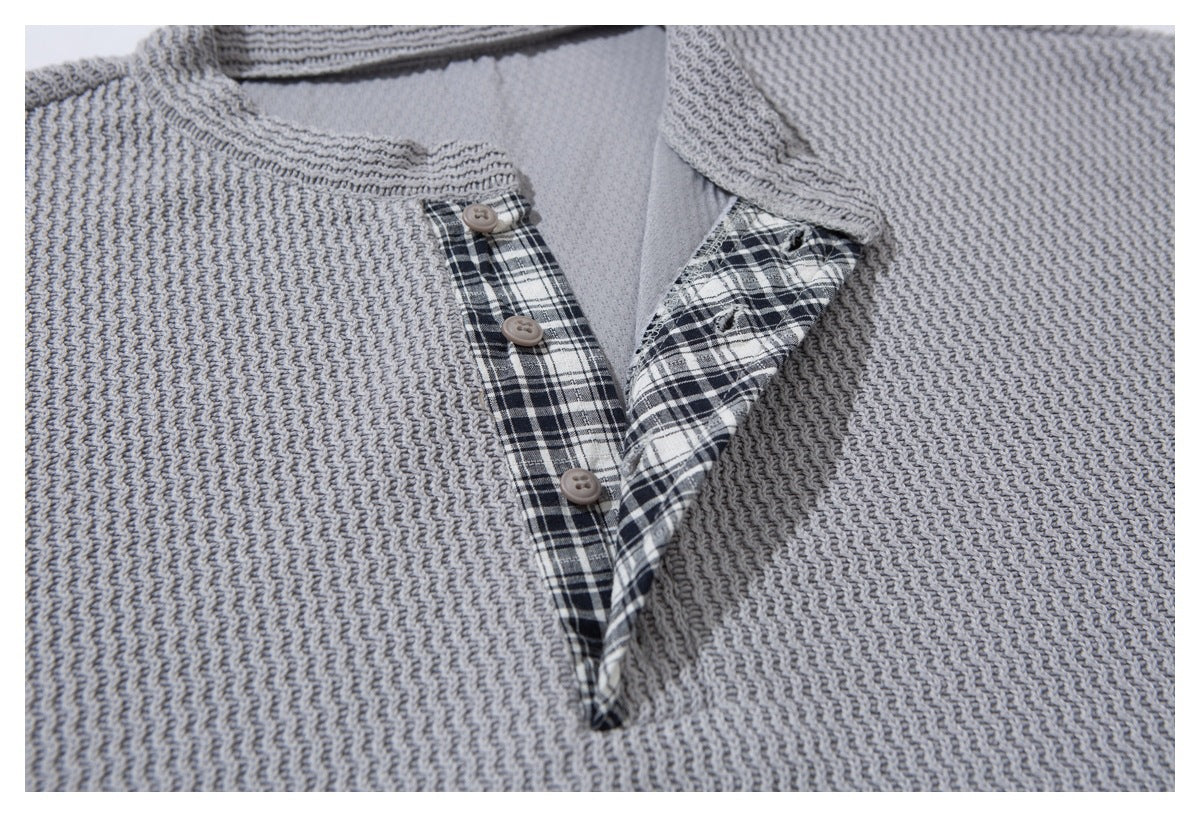 Close-up of the cardigan's open button placket, showing black-and-white plaid trim and gray knit texture.