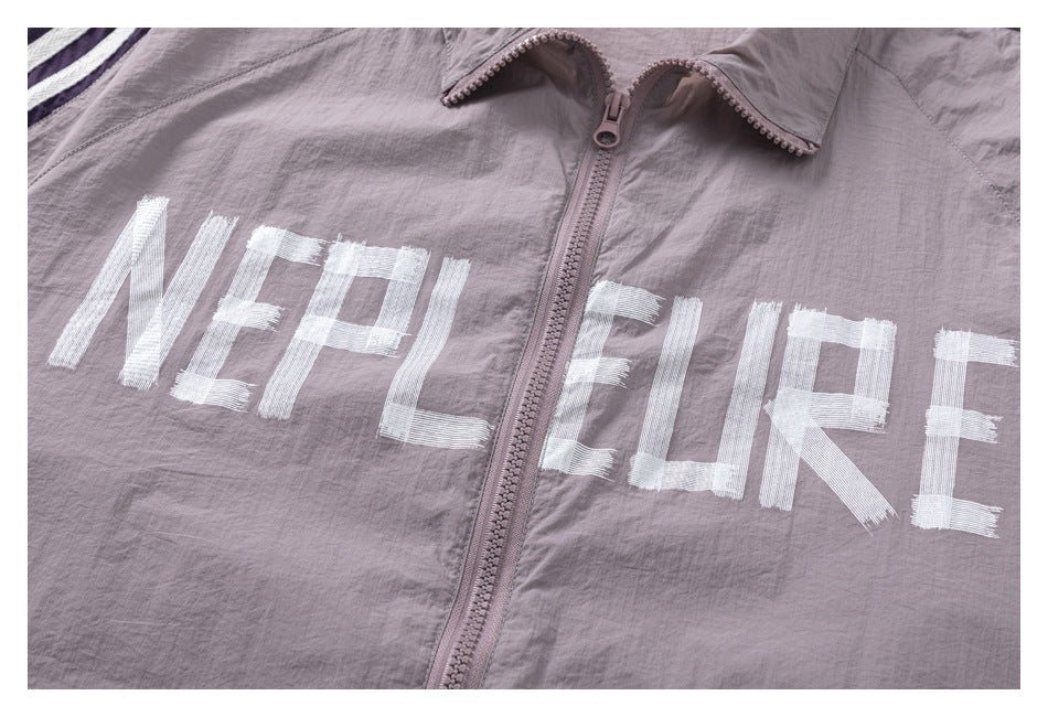 Close-up of large white English lettering across the front of a mauve zip-up jacket.