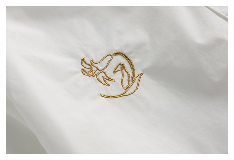 Close-up of a gold embroidered decorative motif on white fabric.
