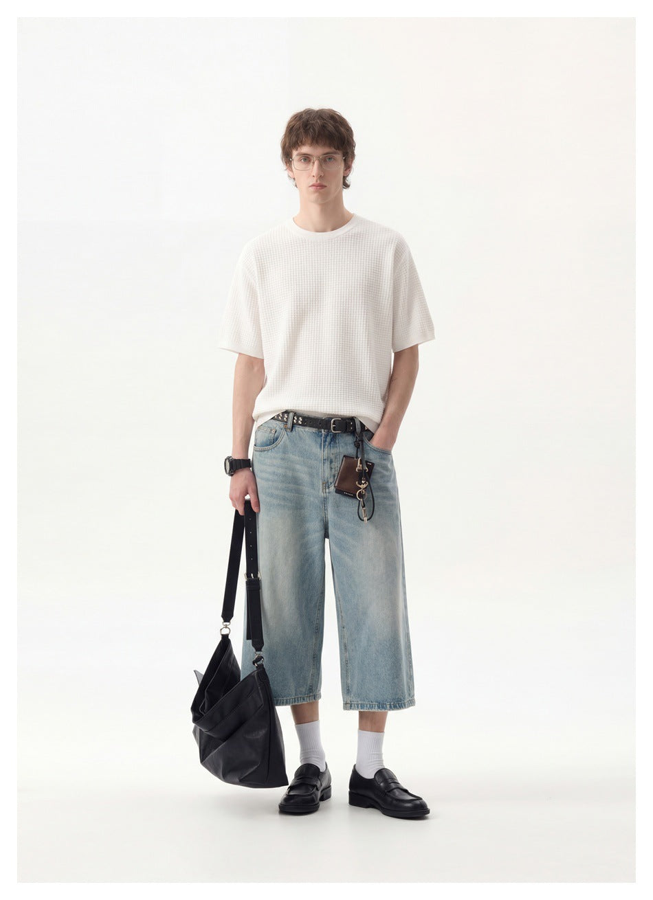 Model wearing a white textured short-sleeve shirt and light-wash denim shorts, carrying a black shoulder bag.