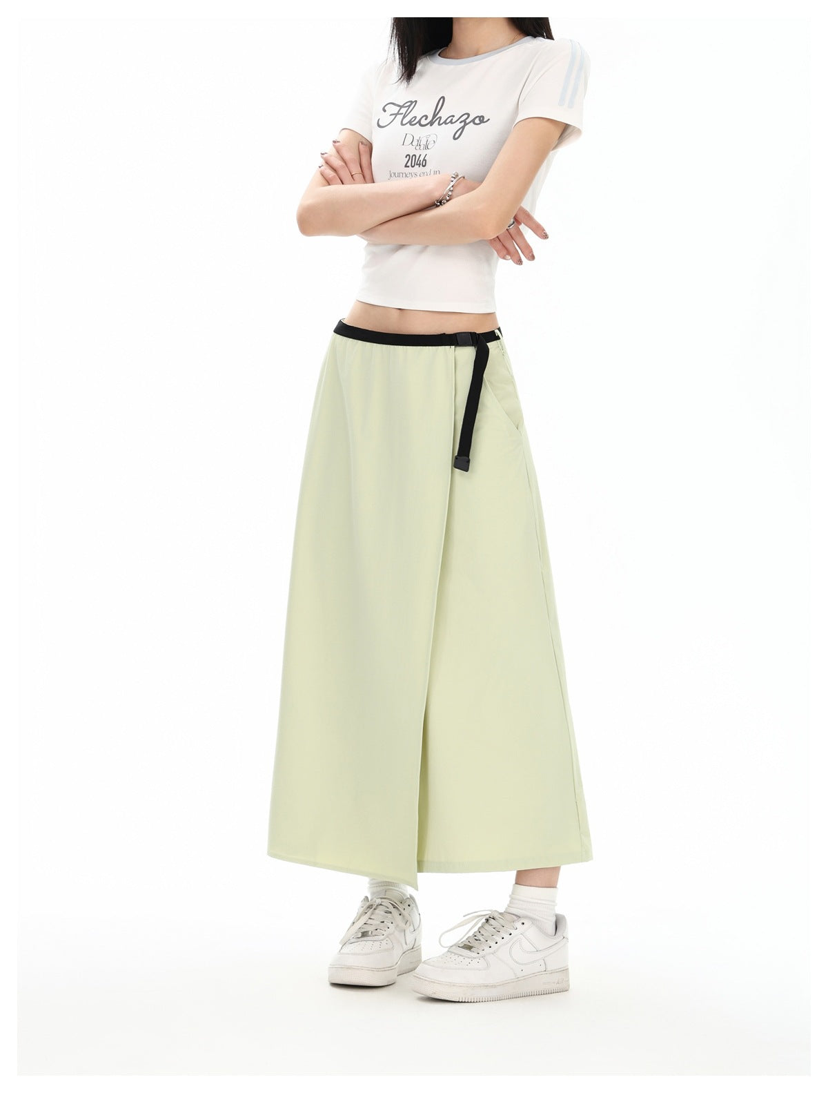 Model wearing a pale yellow-green ankle-length wrap skirt with a black belt over a white graphic T-shirt.