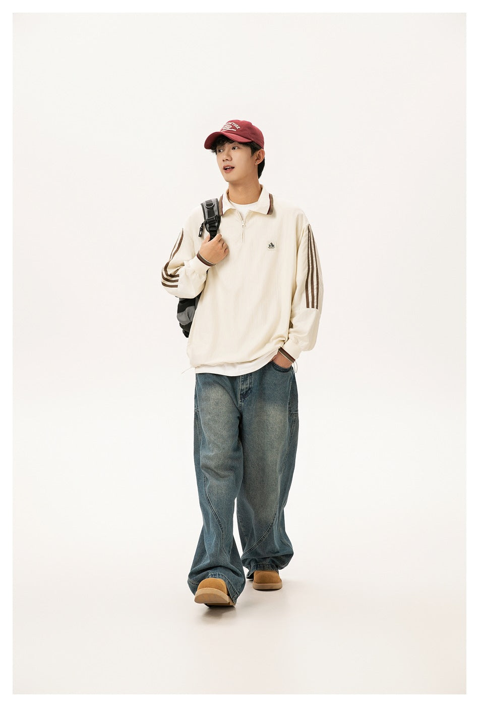 Model walking in a cream quarter-zip polo-collar jacket with brown stripes, red cap and wide-leg jeans