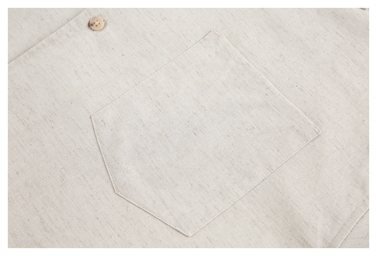 Close-up of an ivory flecked garment with a large stitched pocket and a small beige button.